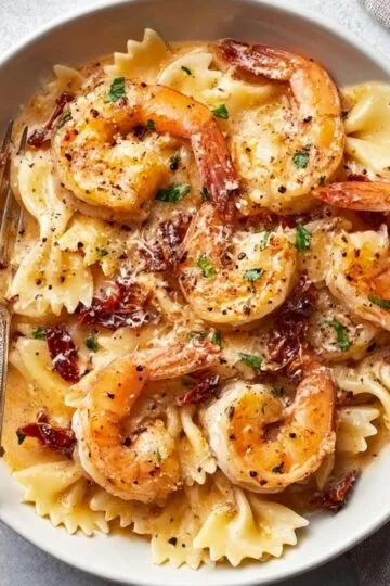 A bowl filled with warm Creamy Shrimp Pasta topped with fresh green herbs and grated cheese.