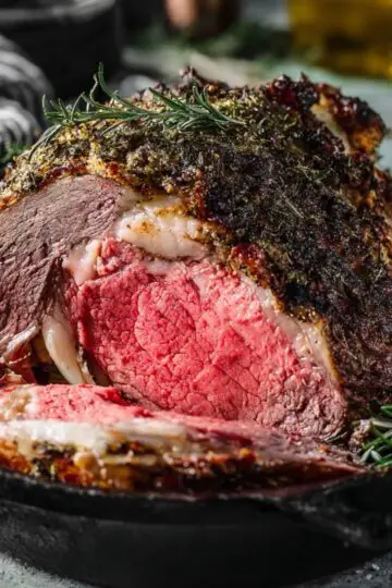 A thick, juicy slice of medium-rare prime rib roast served on a platter with roasted vegetables and a drizzle of rich au jus.
