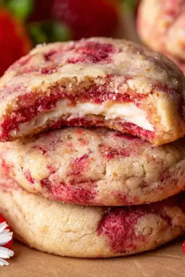 A white plate holds several thick, pink strawberry cookies studded with white chocolate chips, next to a glass of cold milk.