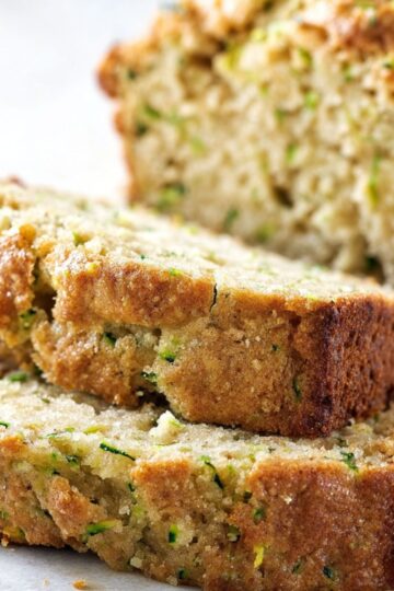 Thick slices of freshly baked, golden-brown zucchini bread rest on a cutting board beside a warm cup of coffee.