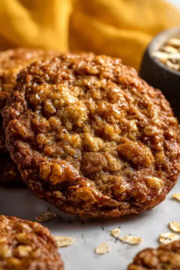 A stack of thick, golden-brown chewy oatmeal cookies rests on a wire cooling rack beside a cold glass of milk.