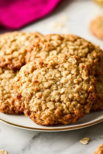 A stack of freshly baked, golden-brown oatmeal cookies studded with chocolate chunks rests on a cooling rack next to a glass of milk.